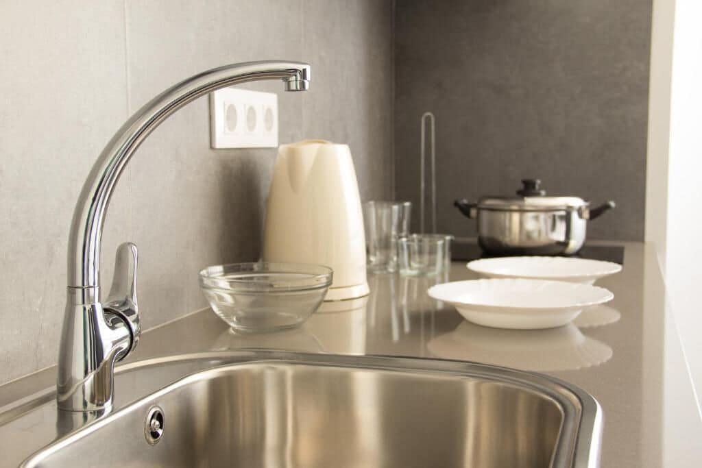 Una cocina moderna con un lavamanos de acero inoxidable, un florero blanco y una olla sobre la encimera.