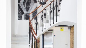 Una escalera moderna con un diseño de candelabro original, una pared blanca con un cuadro abstracto de gran tamaño y una zona de recepción con un banco.
