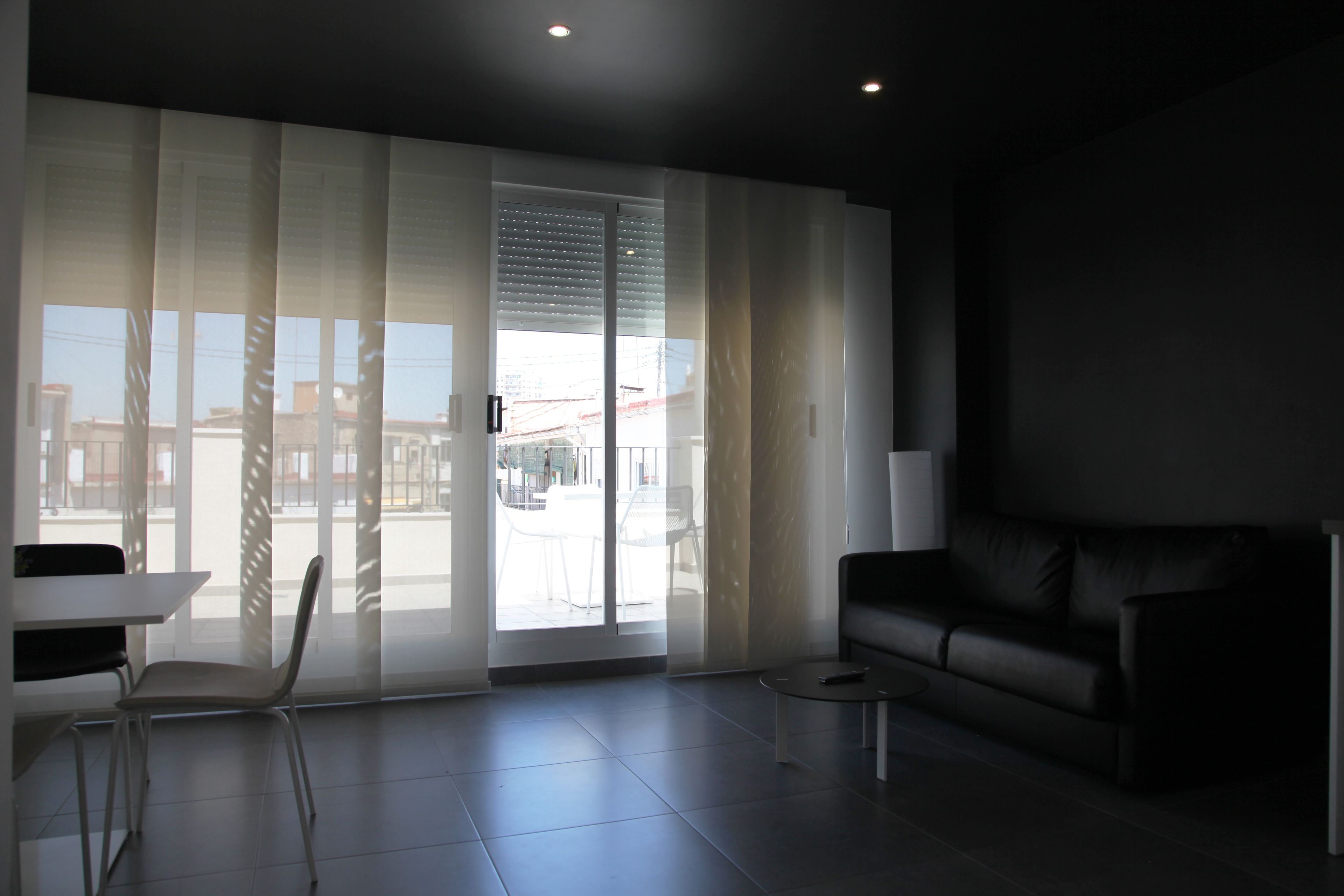 A modern living room with a sliding glass door, a black leather sofa, a white table, and a small round coffee table.