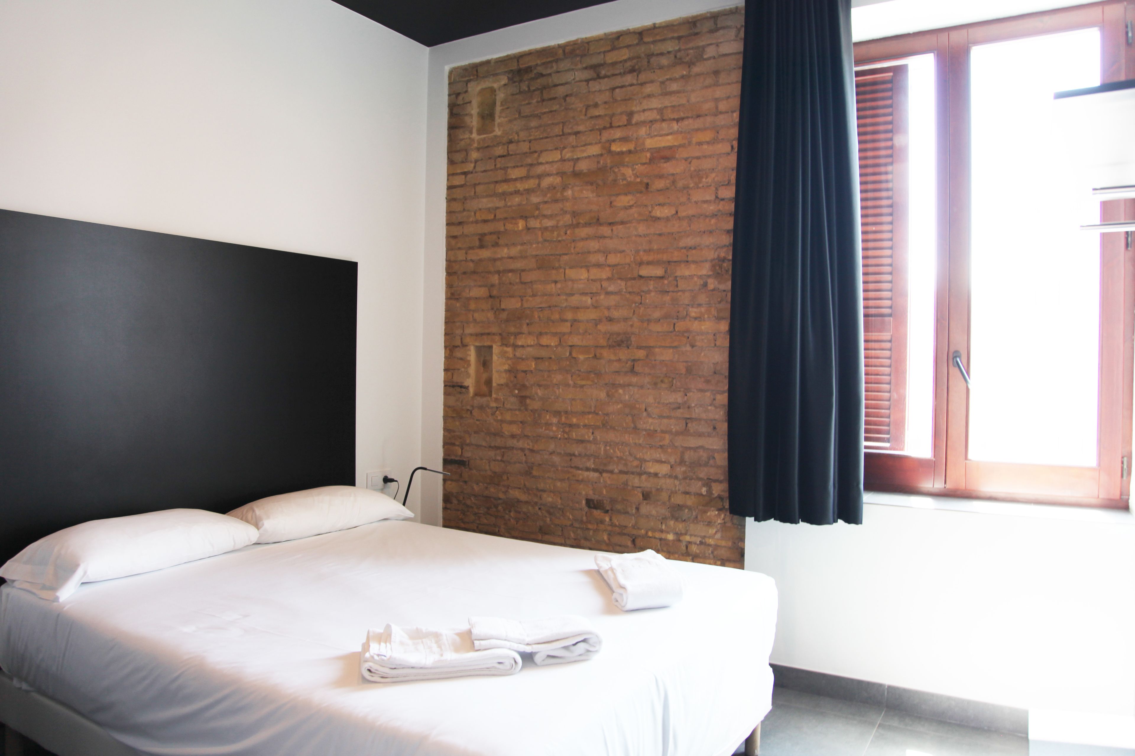 A hotel room with a bed, a brick wall, and a window with blinds.