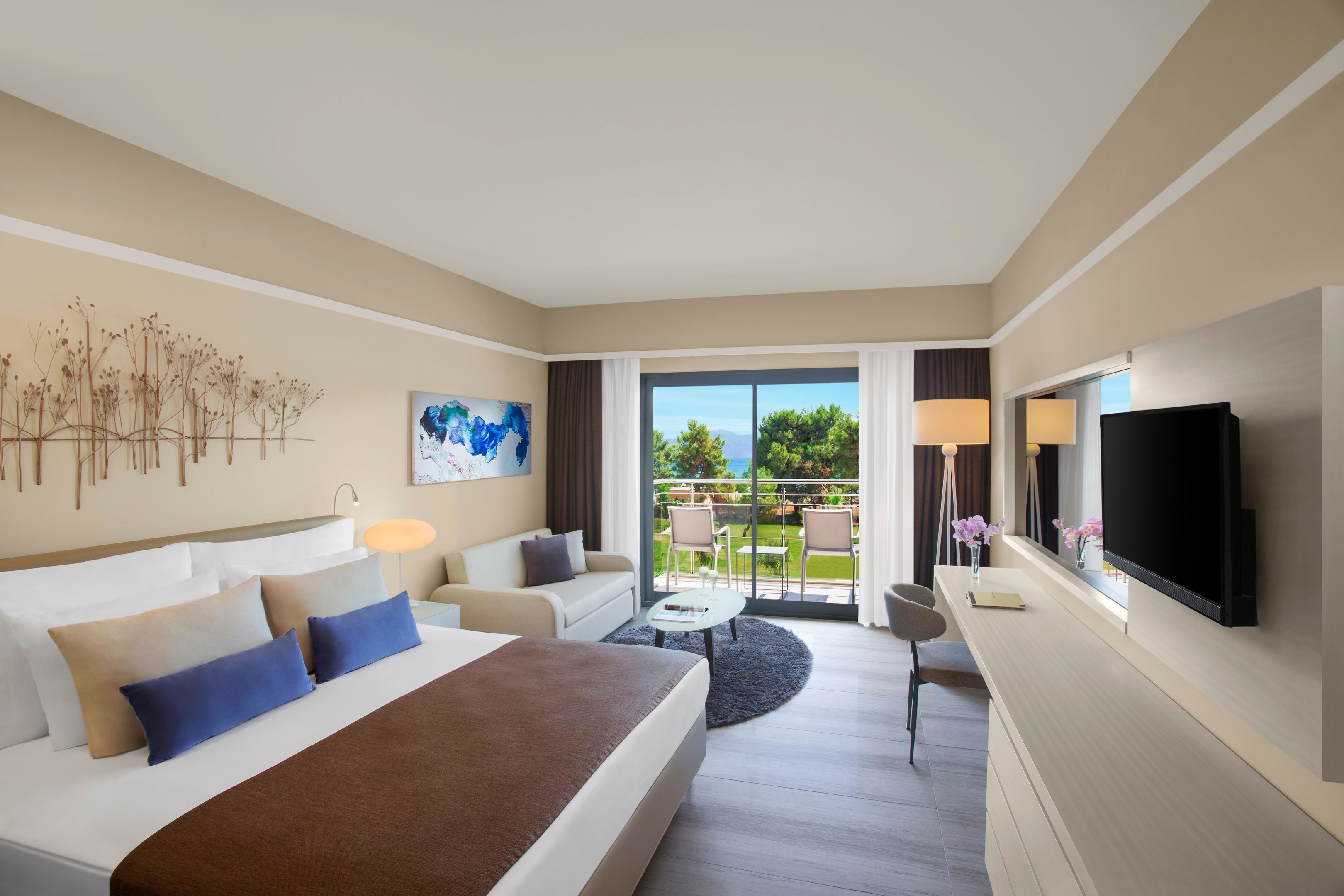 A hotel room with a bed, a sofa, a TV, and a balcony with outdoor furniture.