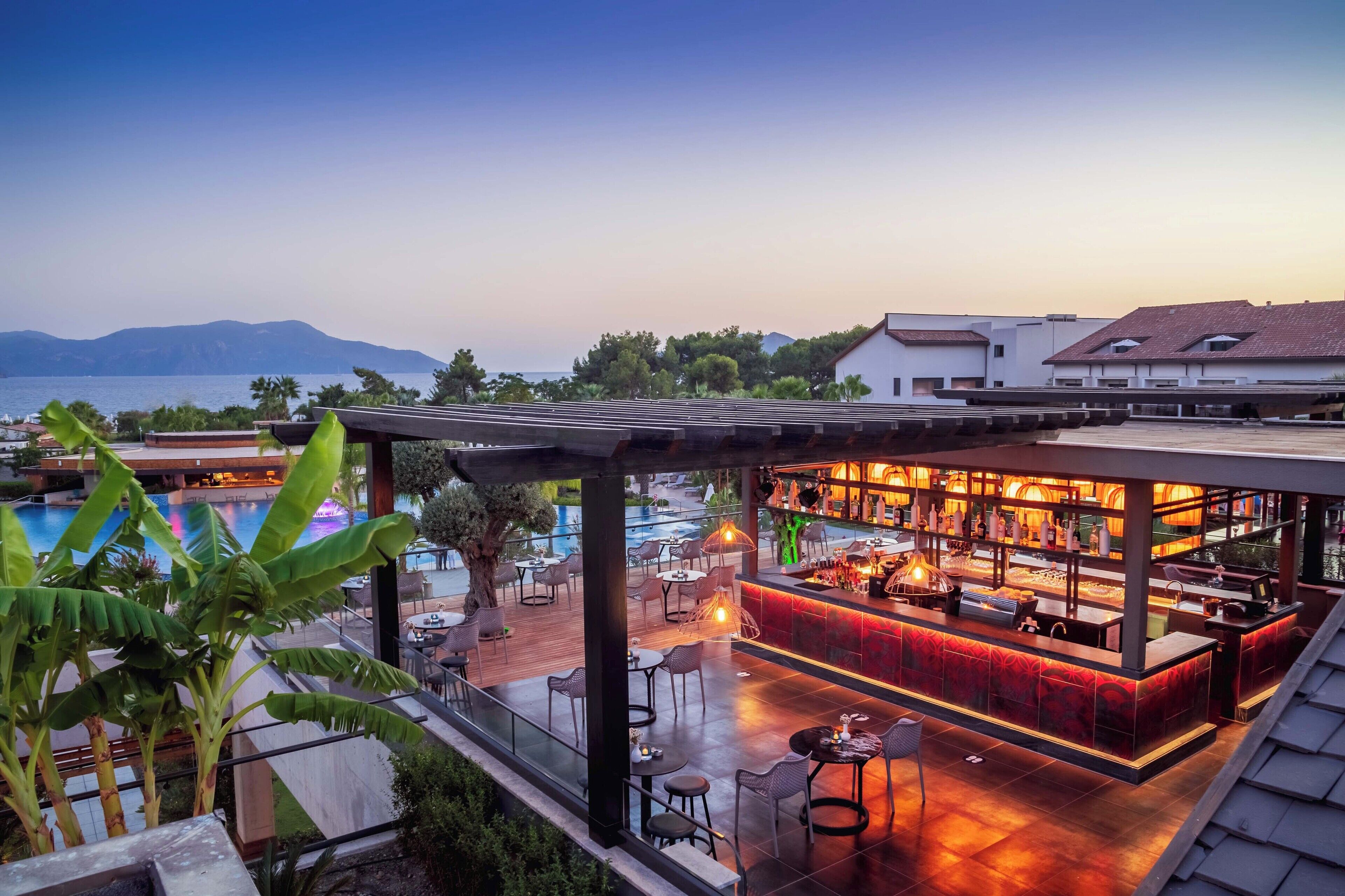 Un bar situé sur le toit, offrant une vue sur la piscine, avec des places assises en plein air et un espace bar.