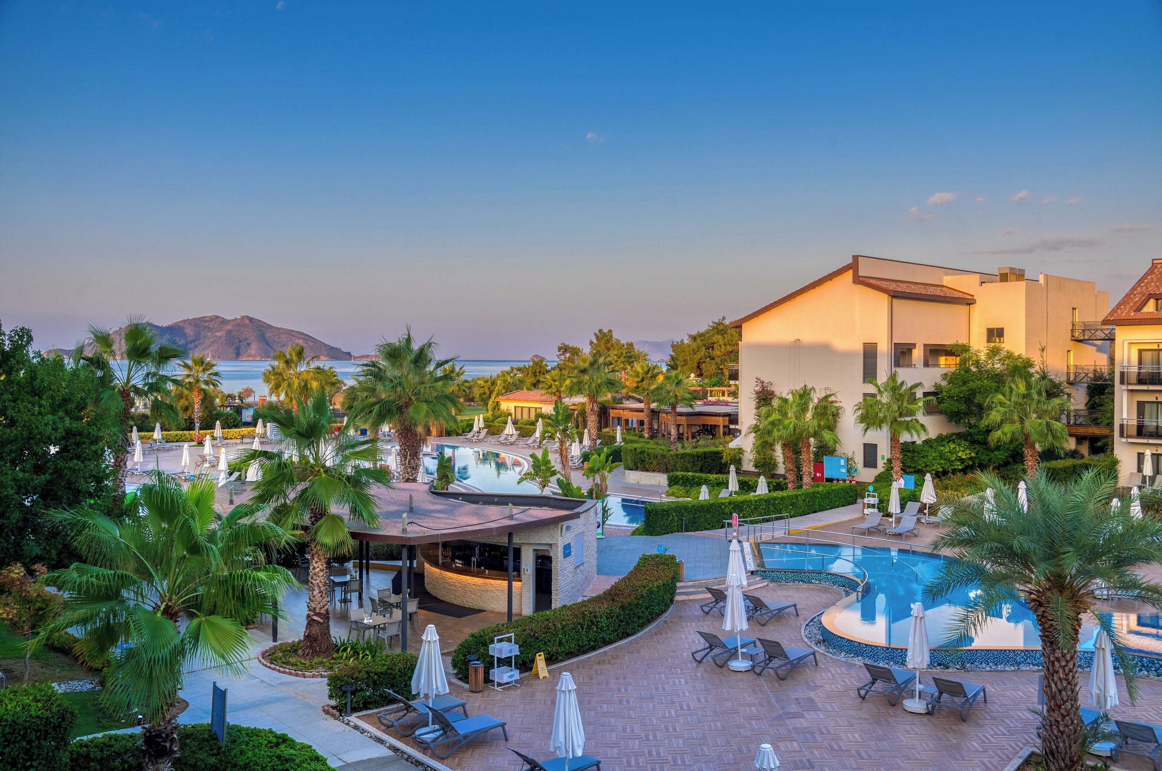 A resort with a swimming pool, lounge chairs, and palm trees.