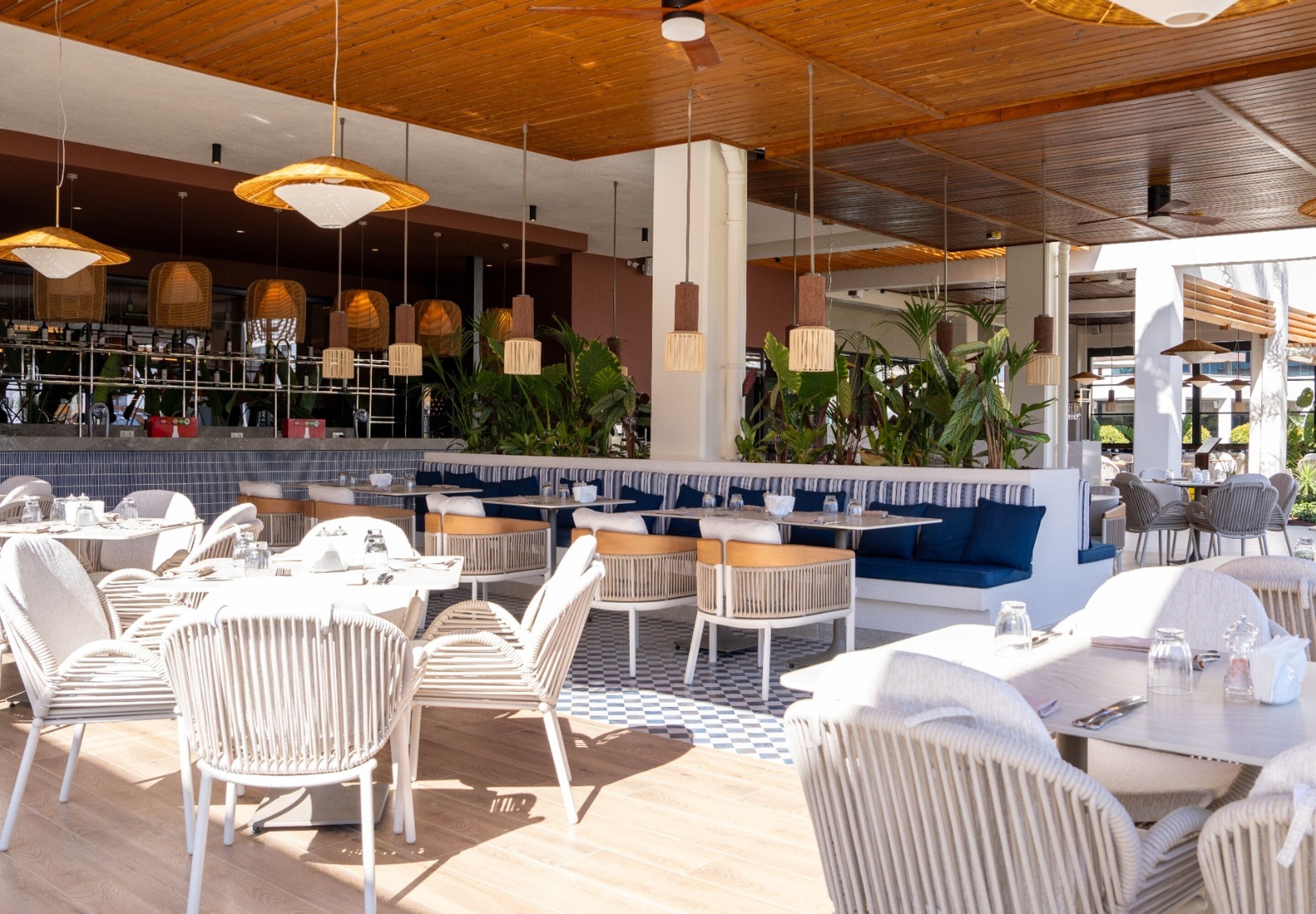 Un espace extérieur aménagé avec des tables et des chaises, un bar en arrière-plan et des lampes suspendues.