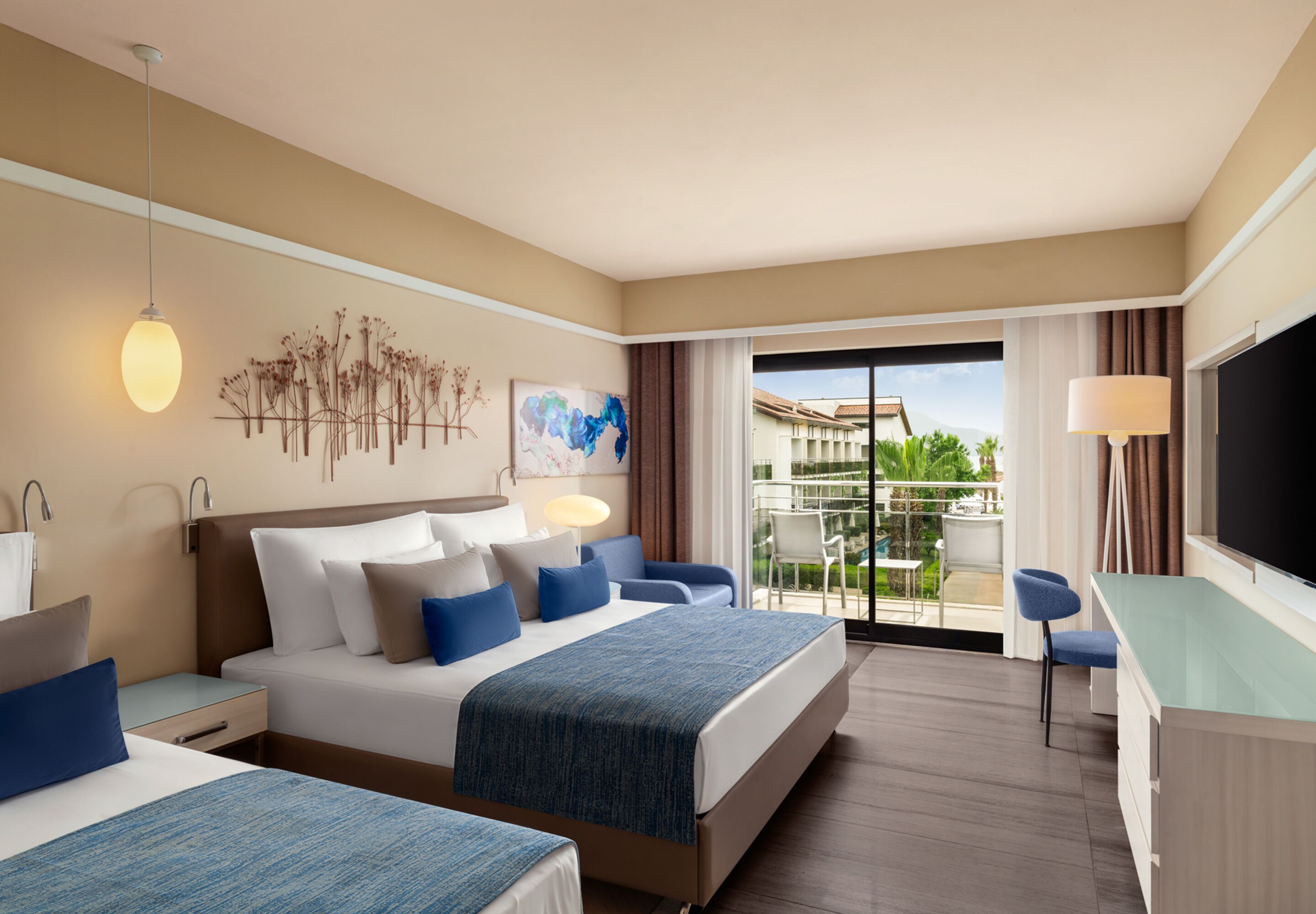 Habitación de hotel con cama, mesitas de noche, escritorio y televisión. Tiene un balcón con vistas al exterior.