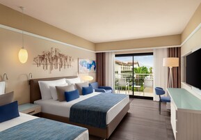 Habitación de hotel con cama, mesitas de noche, escritorio y televisión. Tiene un balcón con vistas al exterior.