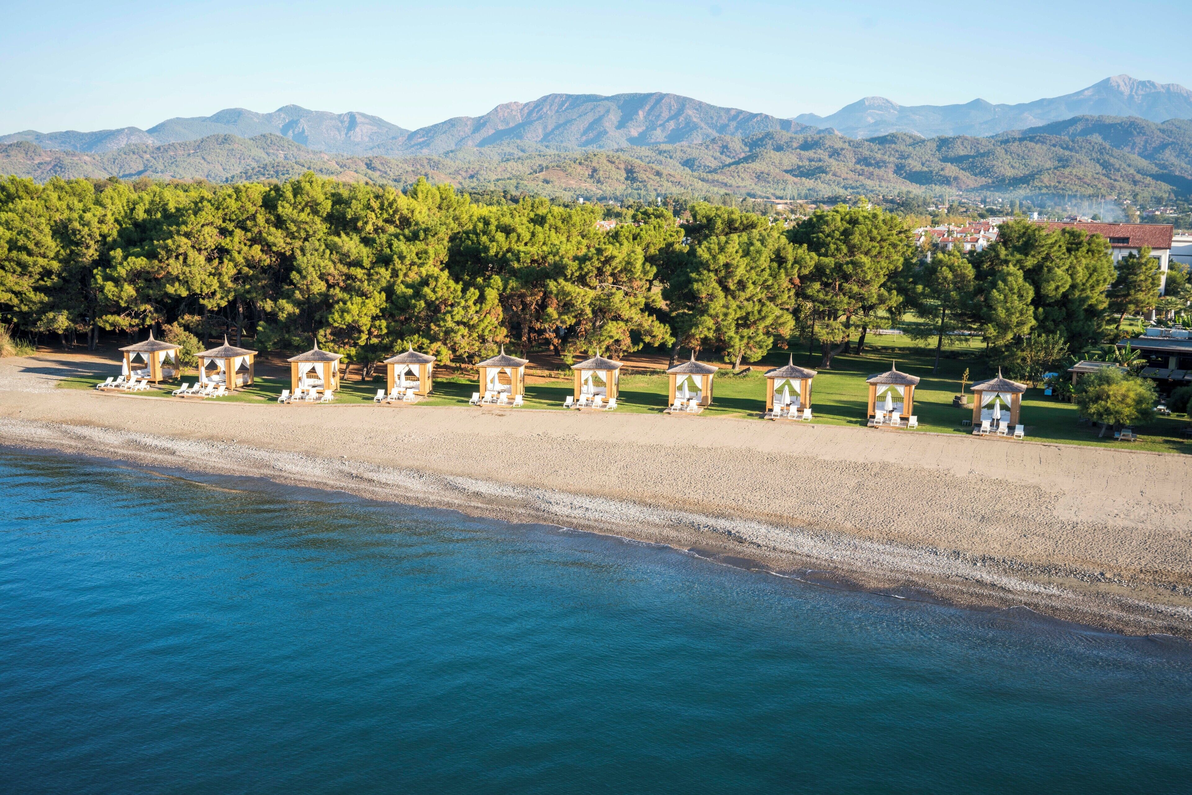 A beach with a row of beach huts and a mountain backdrop.