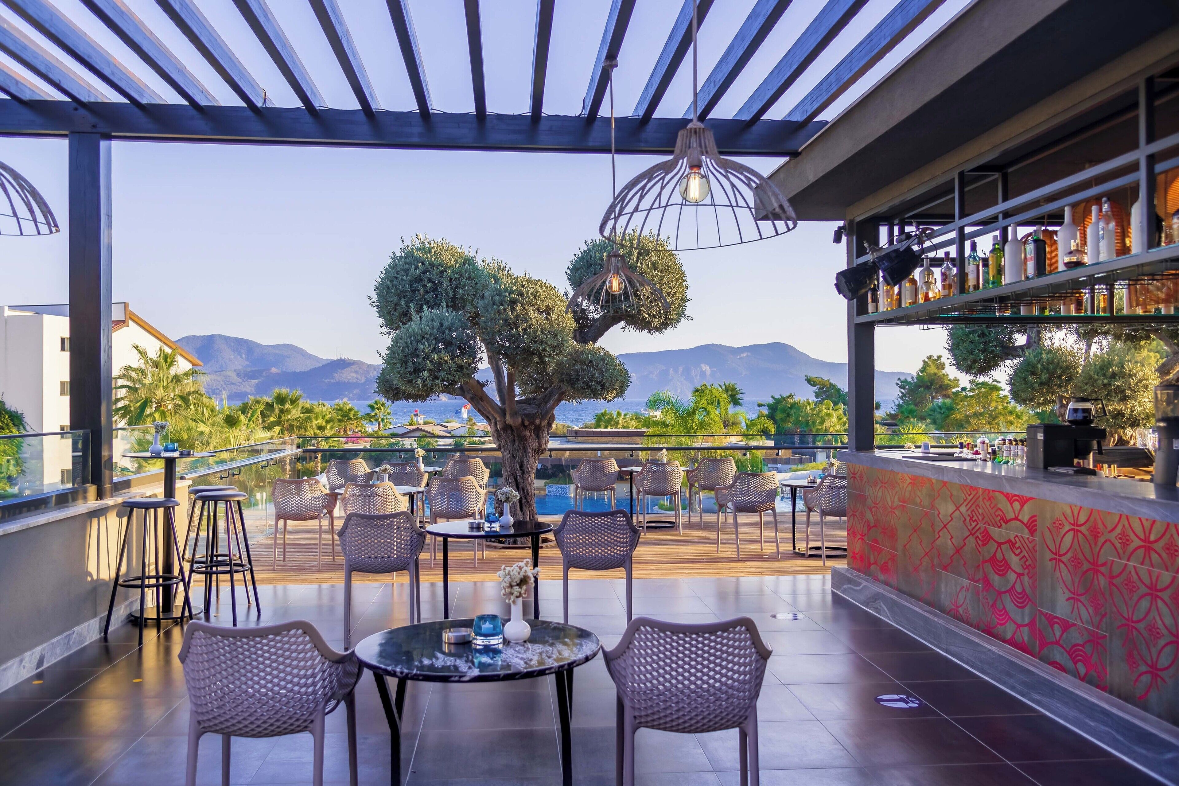 Un bar en la azotea con mesas al aire libre, un árbol y vistas a las montañas.