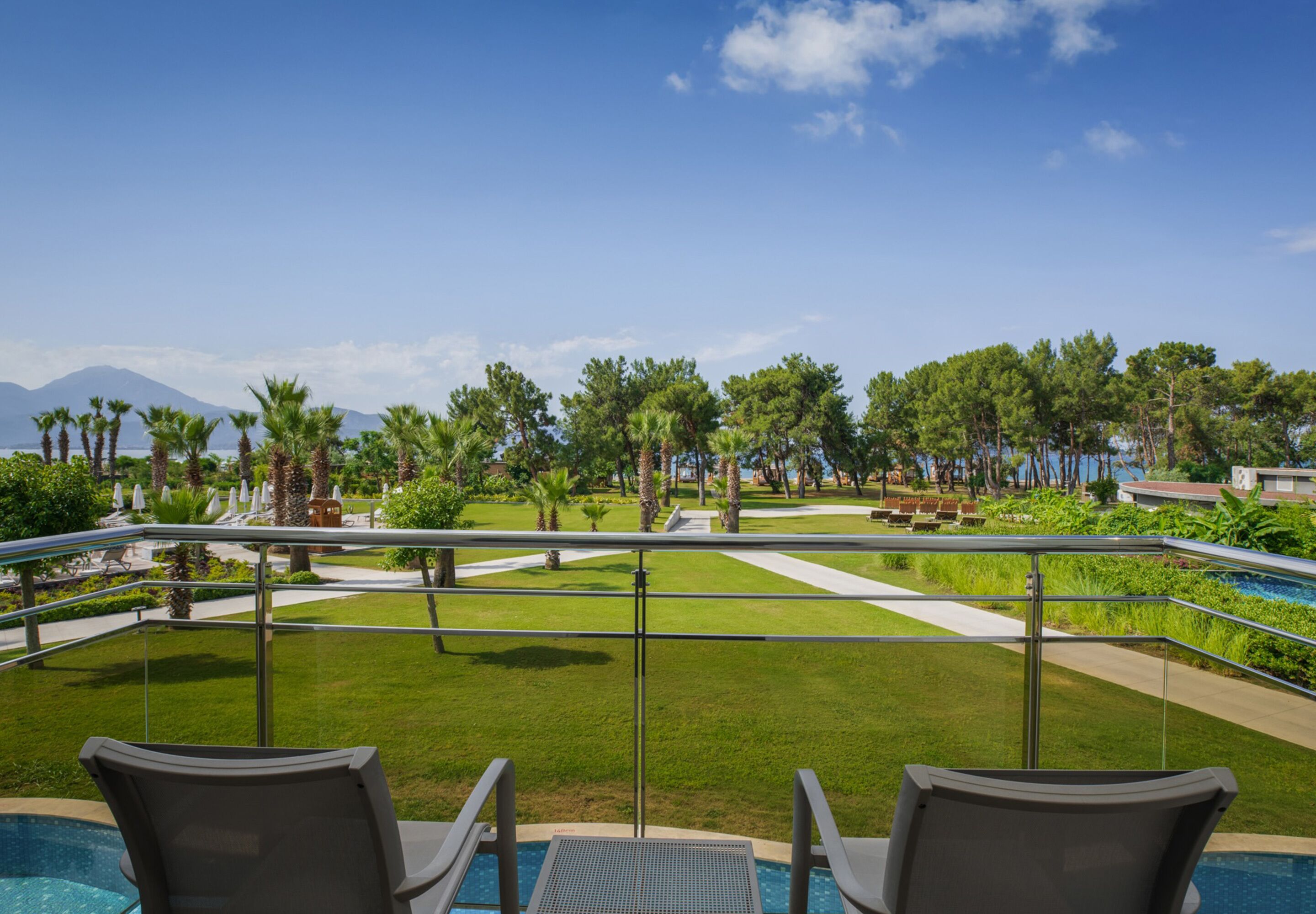 Un área junto a la piscina con sillones de descanso, vista despejada de un jardín ajardinado y una cadena montañosa distante.