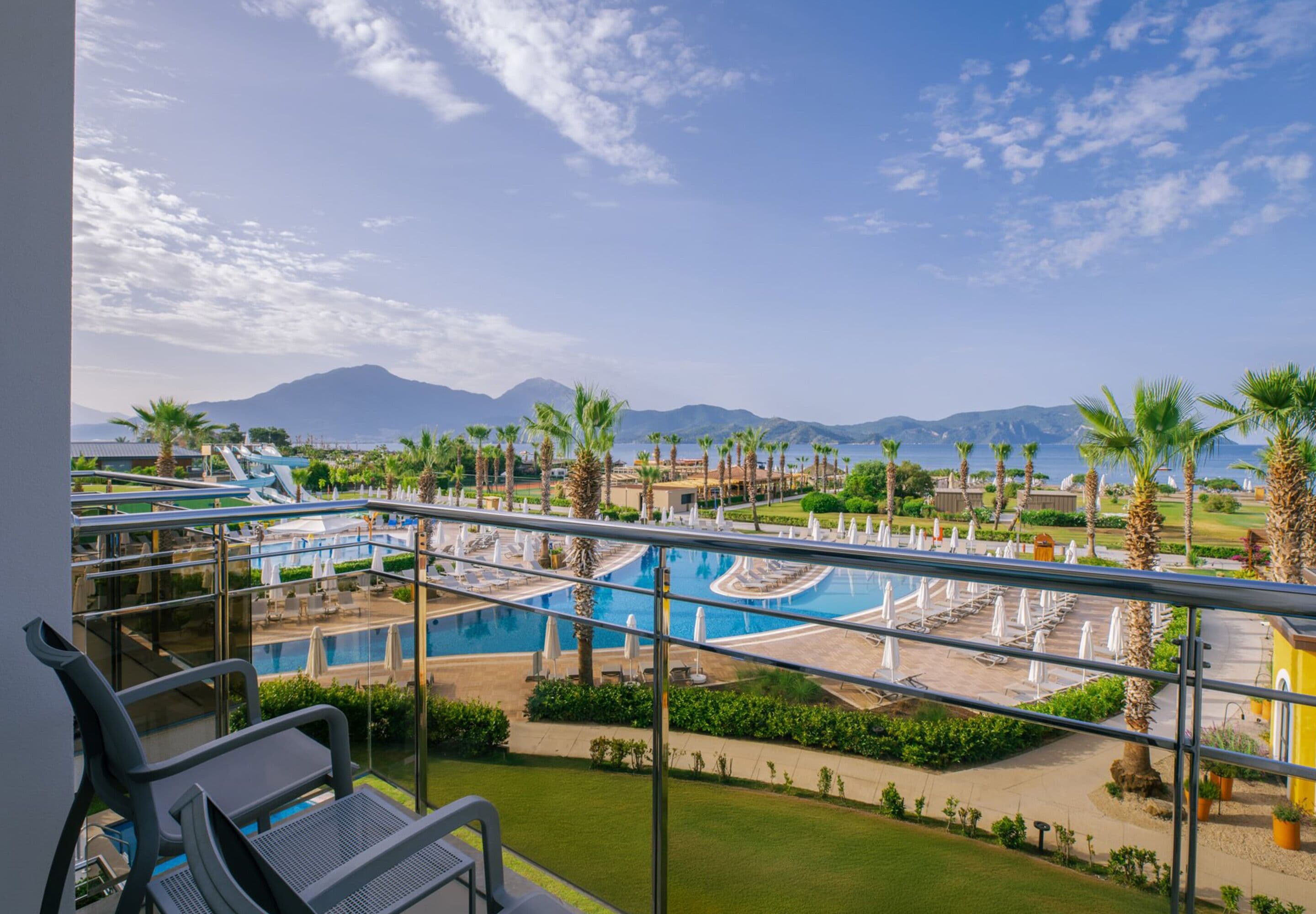 A resort with a pool area, palm trees, and mountains in the background.