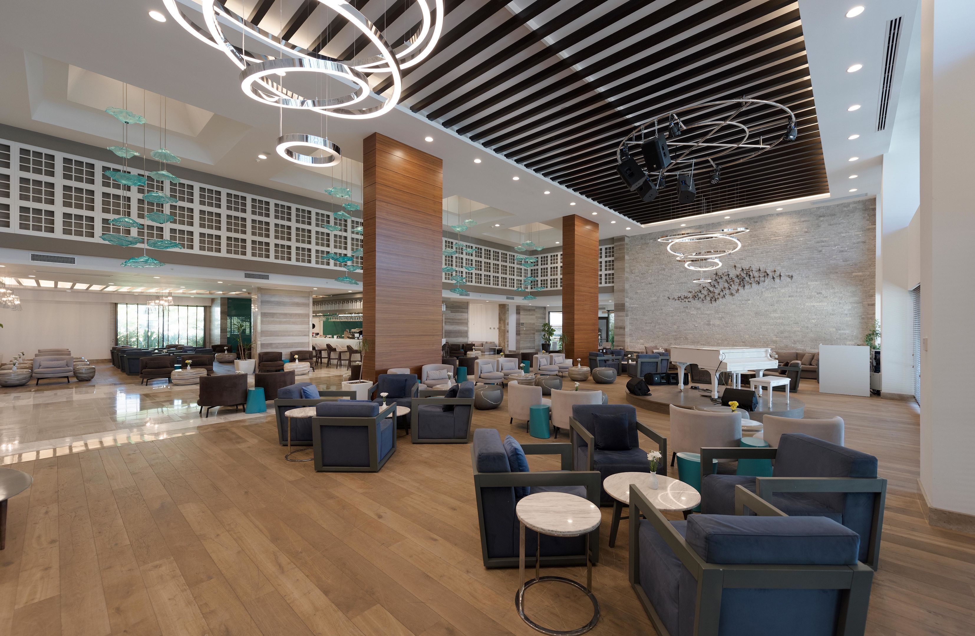 A spacious lobby with modern furniture, a high ceiling with circular light fixtures, and a large wall with a geometric design.