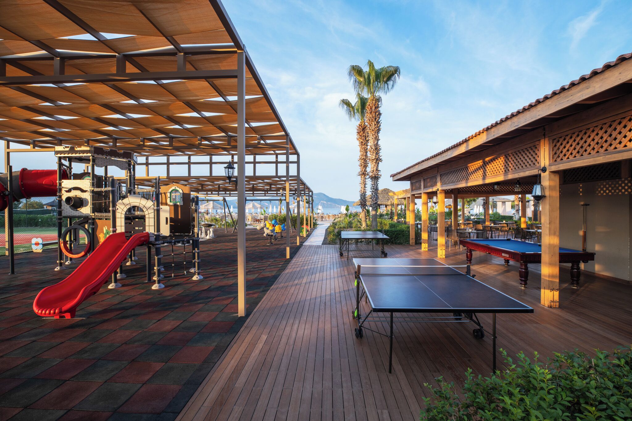An outdoor recreational area with a ping pong table, a red slide, and exercise equipment.