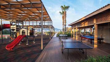 An outdoor recreational area with a ping pong table, a red slide, and exercise equipment.