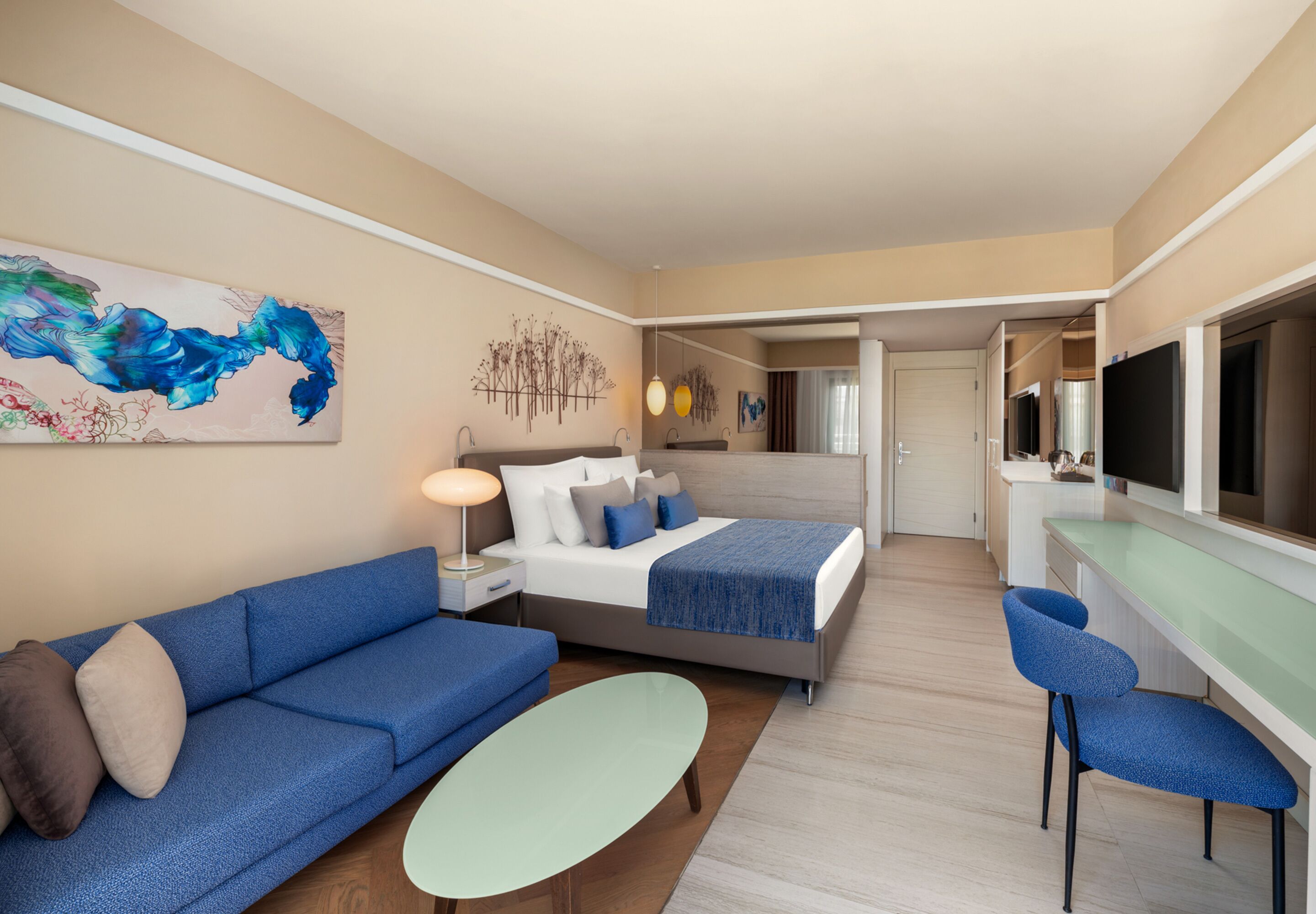 Una habitación de hotel moderna con cama, sofá, sillones, un comedor y televisor.