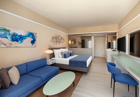 A modern hotel room with a bed, sofa, and chairs, a dining area, and a TV.