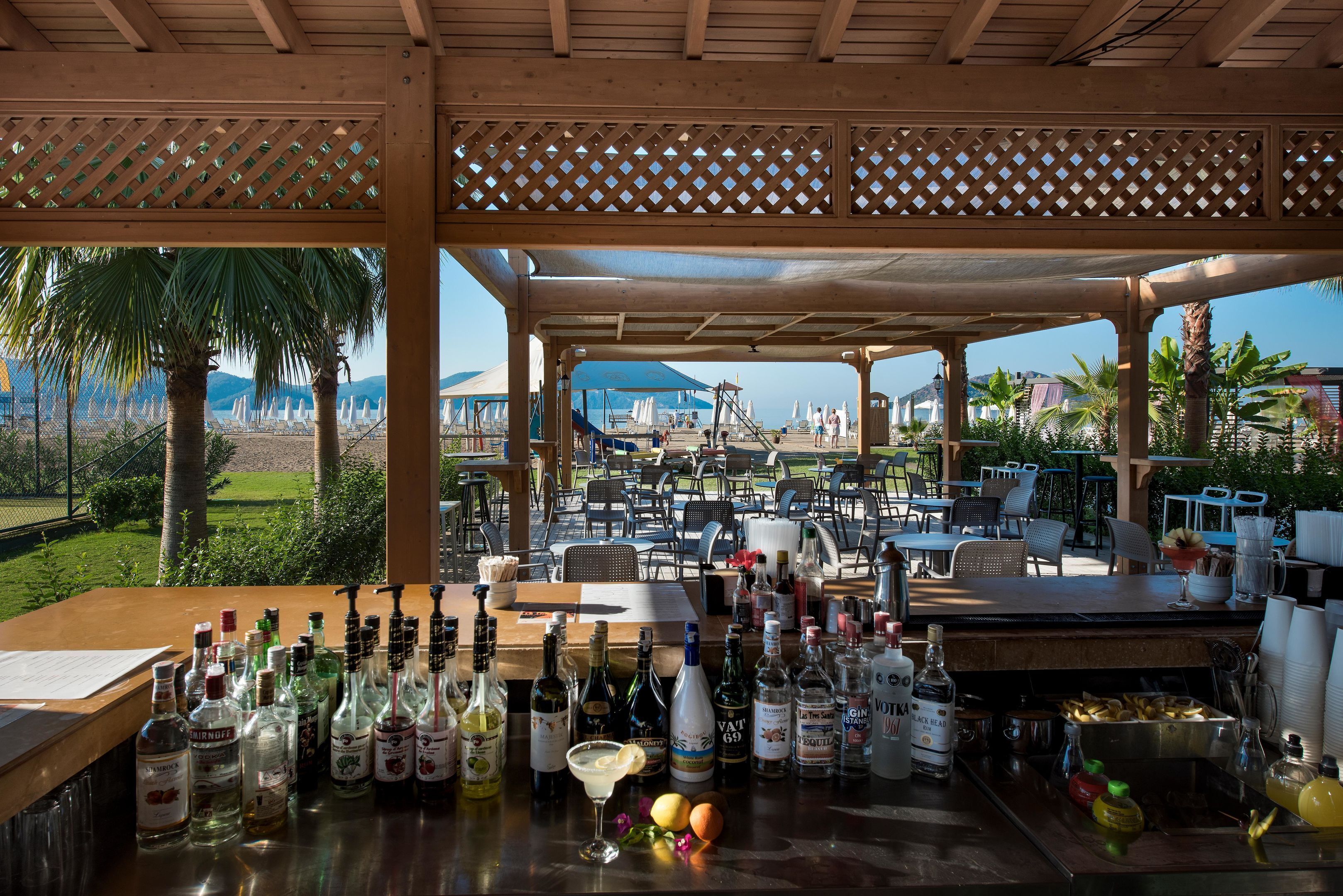 An outdoor bar area with a view of the beach and mountains, equipped with a variety of liquor bottles and a grill.