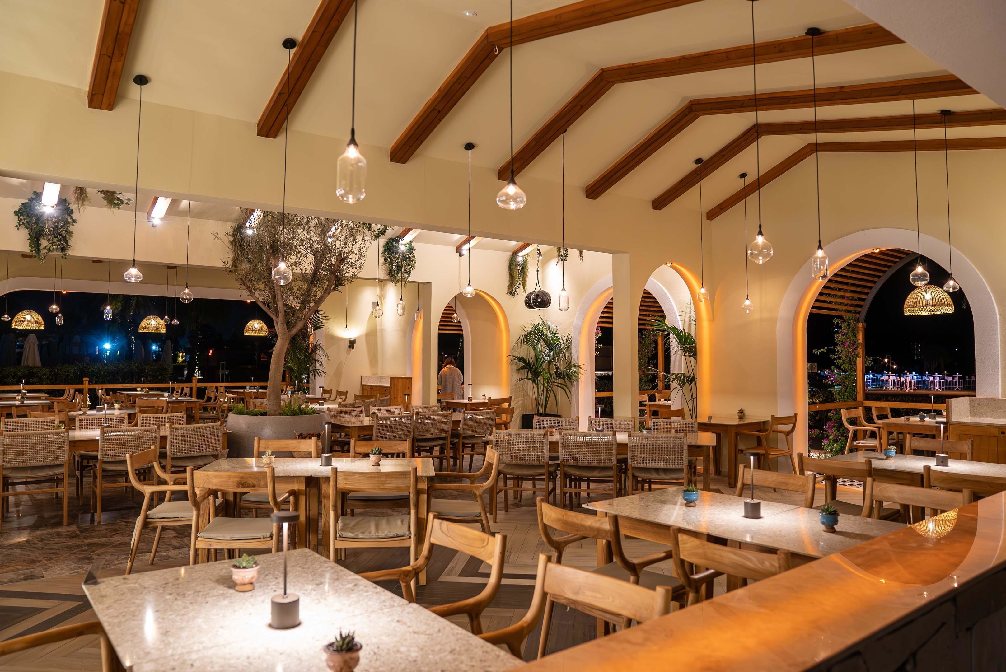 A restaurant with wooden tables and chairs, hanging pendant lights, and arched windows.
