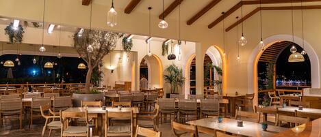 A restaurant with wooden tables and chairs, hanging pendant lights, and arched windows.