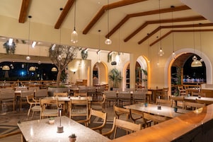 A restaurant with wooden tables and chairs, hanging pendant lights, and arched windows.