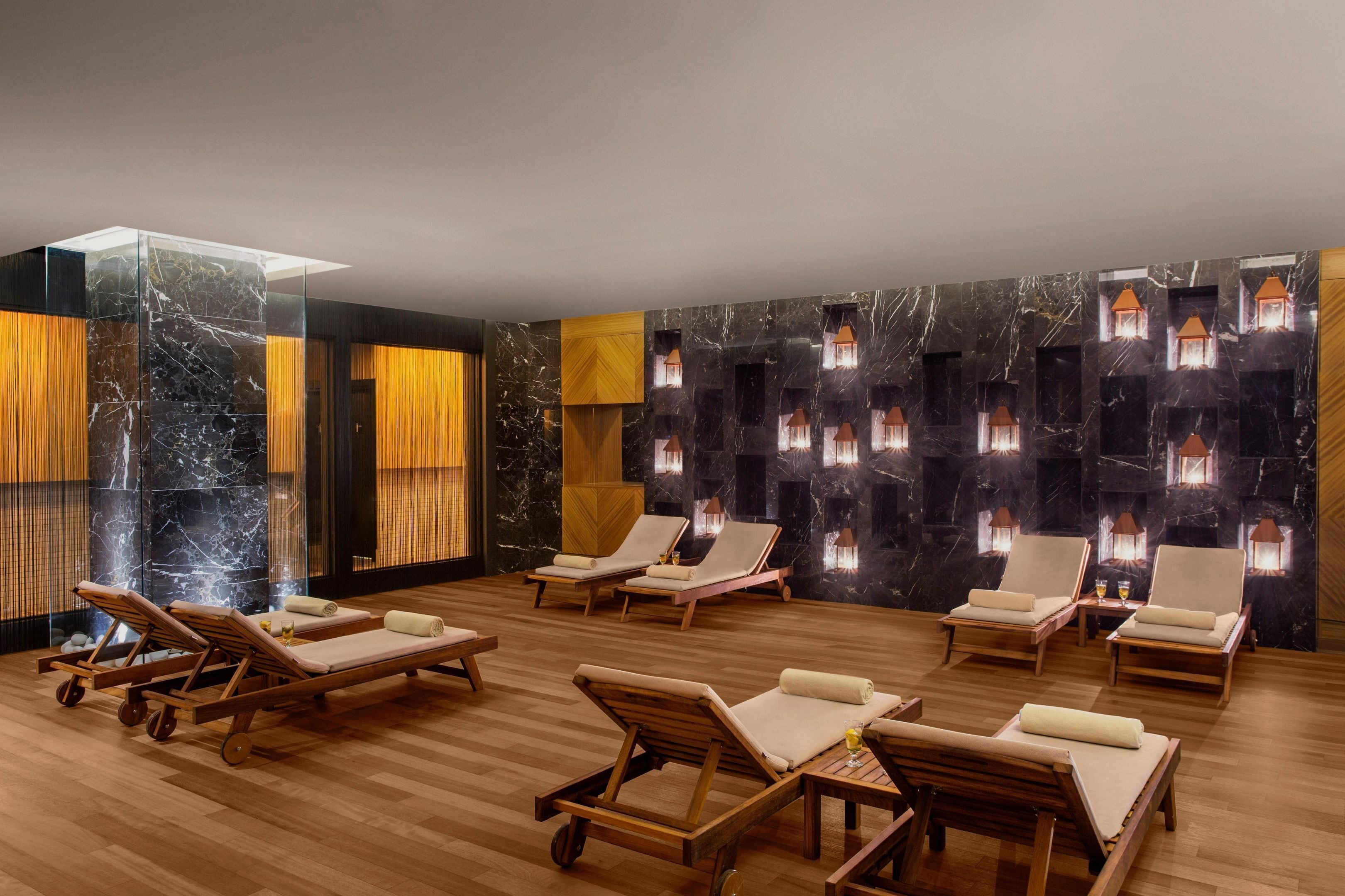 A spa room with wooden loungers, a glass partition, and wall-mounted lights.