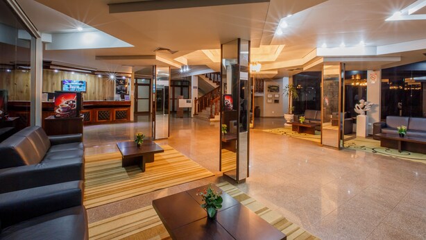 A spacious lobby with a modern design, featuring a seating area with sofas and a coffee table, a television mounted on the wall, and a staircase leading to an upper level. - Olinda Hotel e Eventos (Toledo)