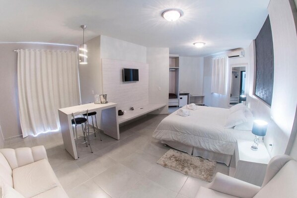 Une chambre d’hôtel moderne équipée d’un lit, d’un bureau avec deux chaises, d’une télévision et d’un dressing.