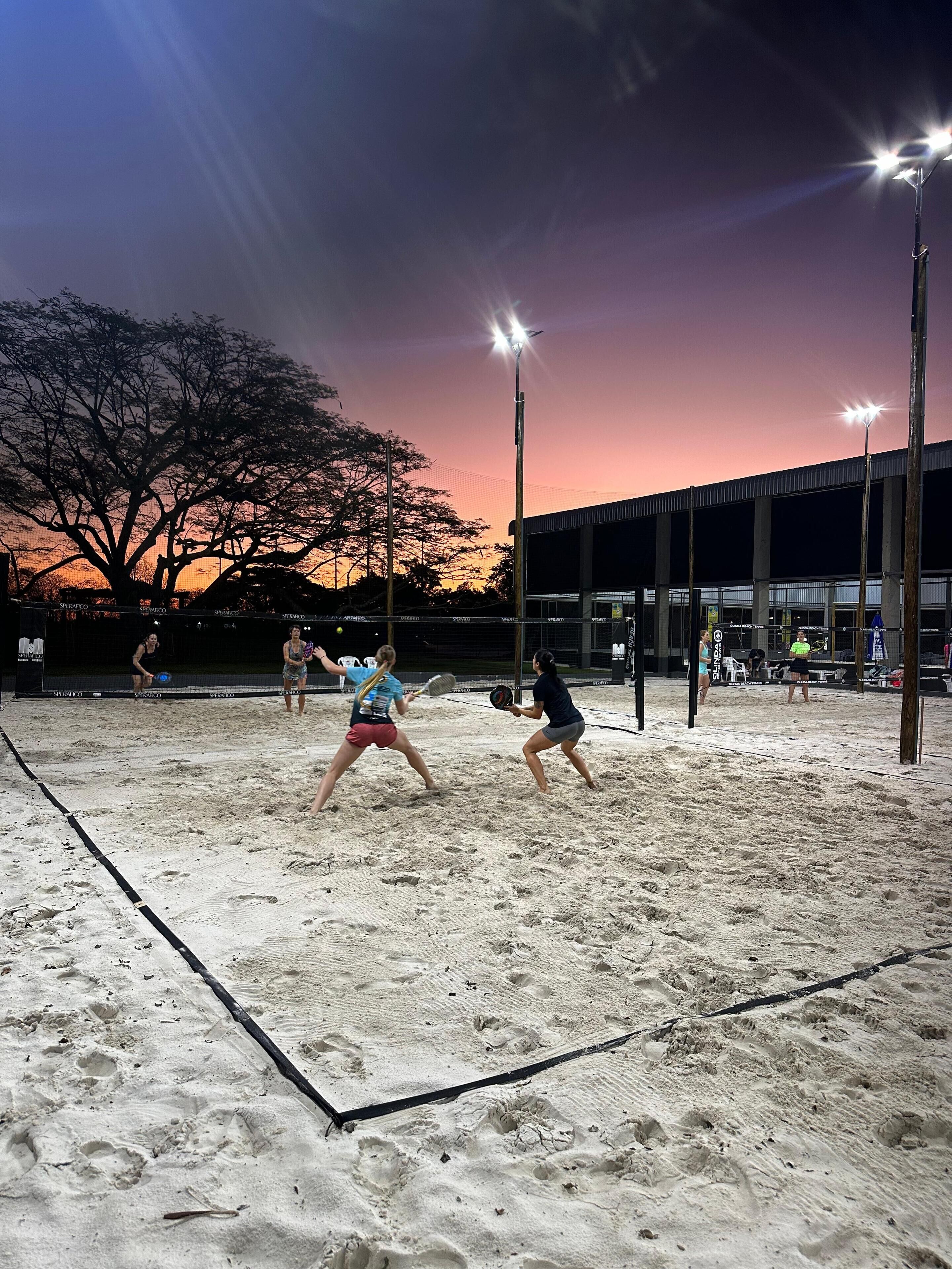 A volleyball game on a sandy court with a sunset in the background.