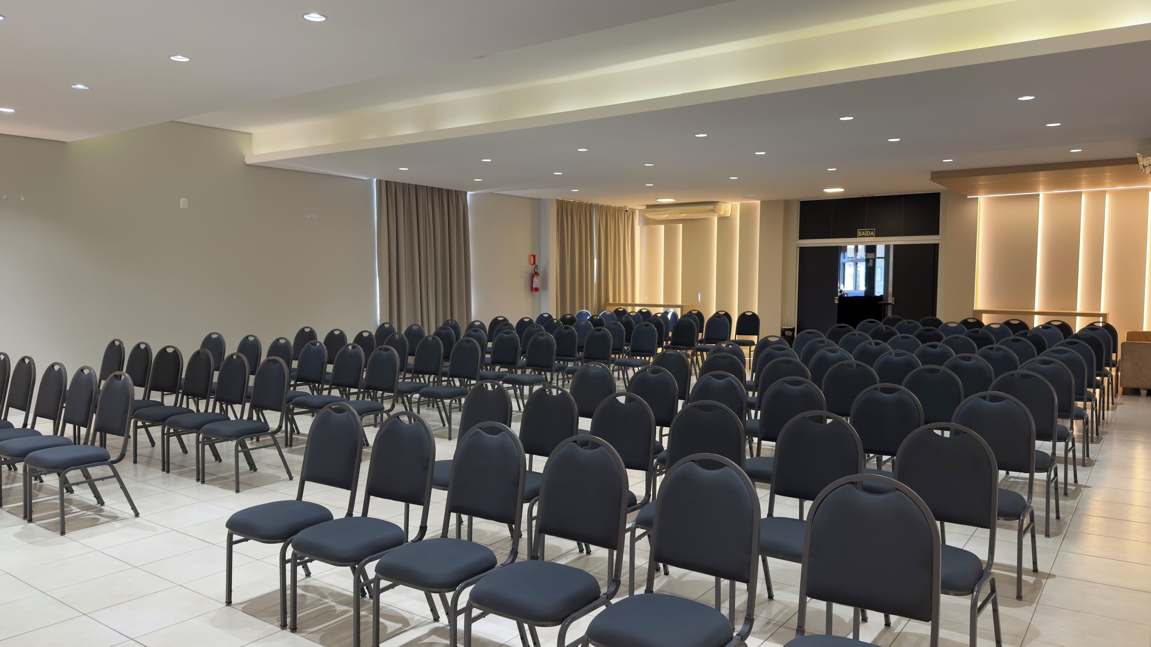 A conference room with rows of chairs, a podium, and a large window with curtains.