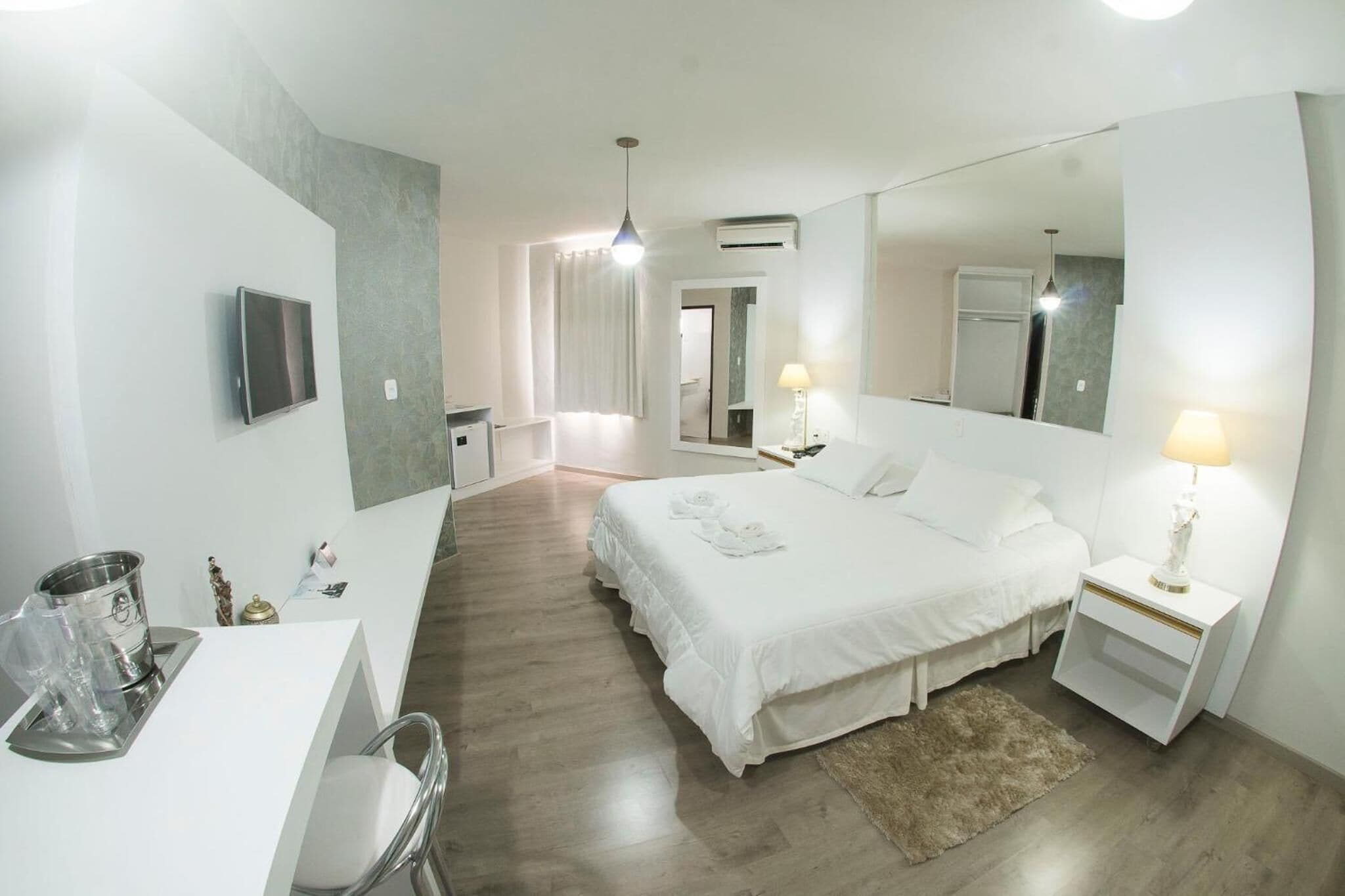 Een hotelkamer met een bed, nachtkastjes, een bureau, een stoel, een grote spiegel en uitzicht op de gang.