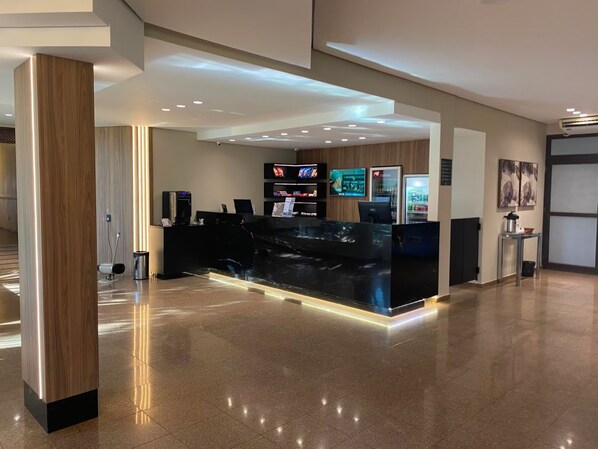 A modern reception area with a black reception desk, multiple flat-screen TVs, and a clean, polished floor. - Olinda Hotel e Eventos (Toledo)