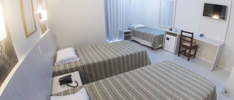 Habitación de hotel con dos camas individuales, un escritorio con silla, televisión y un refrigerador pequeño.