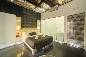 Una habitación de hotel moderna con una cama grande, una mesita de noche, una pared con diseños geométricos y una puerta corredera con texto informativo.