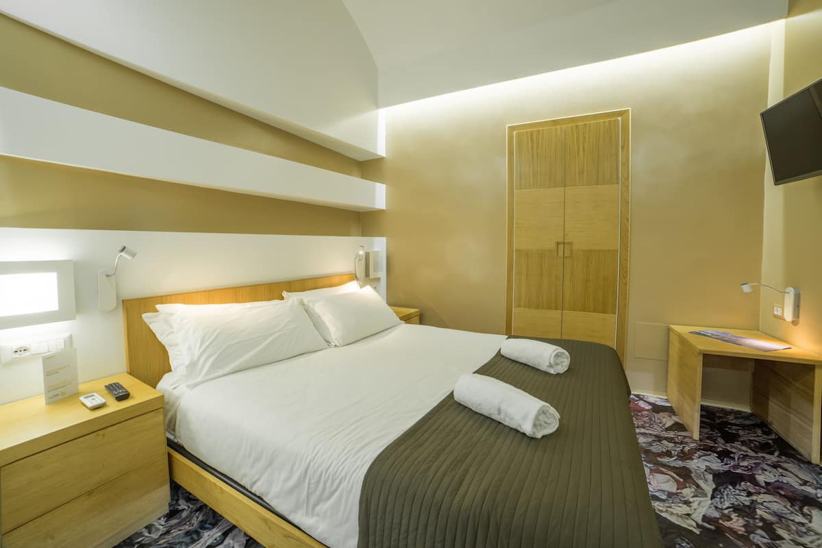 Ein Hotelzimmer mit Bett, Nachttisch und Fernseher an der Wand.