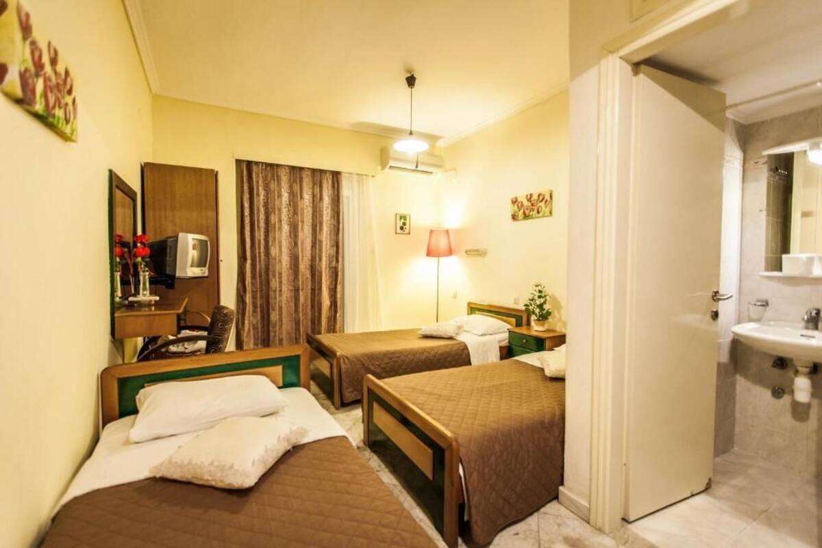 Ett hotellrum med två sängar, ett skrivbord med en dator, en lampa och ett badrum med handfat.