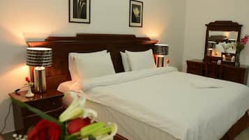 A neatly made bed with white linens, two bedside lamps, a nightstand with a vase of flowers, and a mirror on the wall.