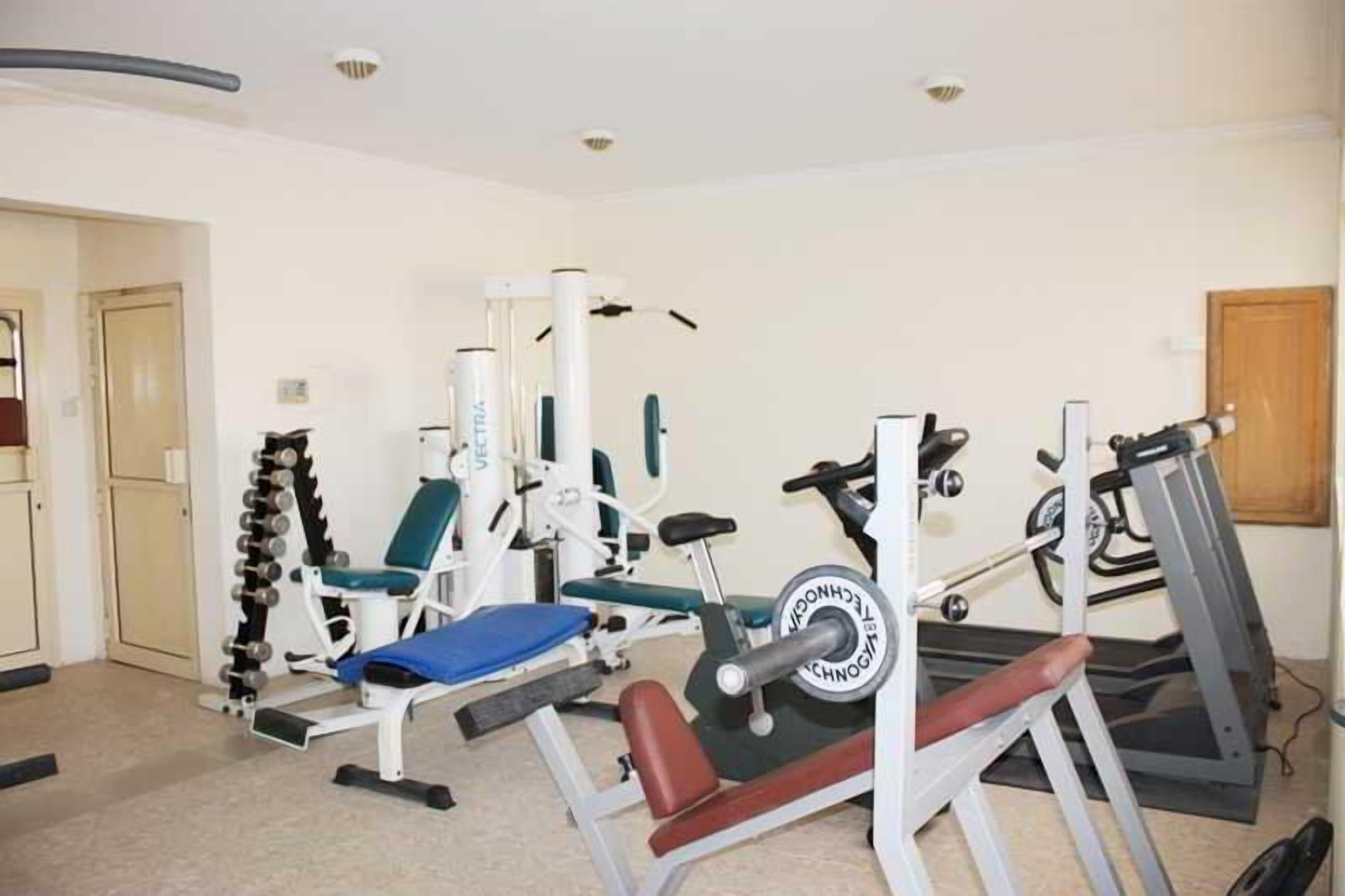 Een huisgymnasium met diverse fitnessapparaten, waaronder een bankdrukrek, een gewichtsstapelaar en een loopband.