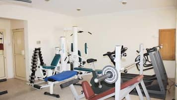 Een huisgymnasium met diverse fitnessapparaten, waaronder een bankdrukrek, een gewichtsstapelaar en een loopband.