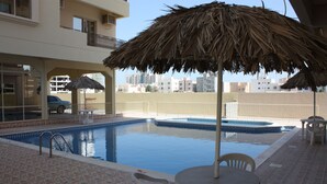 Una piscina con un quiosco de techo de paja, una silla de descanso y una mesa.