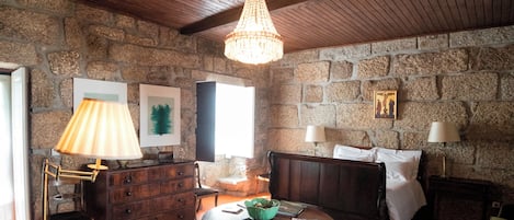 A cozy room with a stone wall, wooden ceiling, a round table, a sofa, and a lamp.