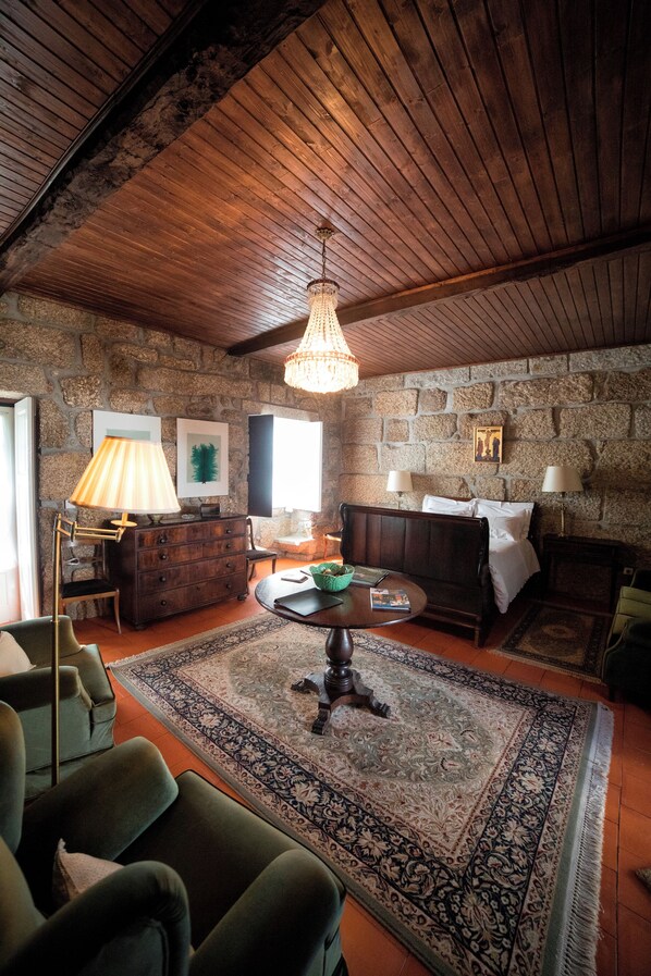A cozy room with a stone wall, wooden ceiling, a round table, a sofa, and a lamp.