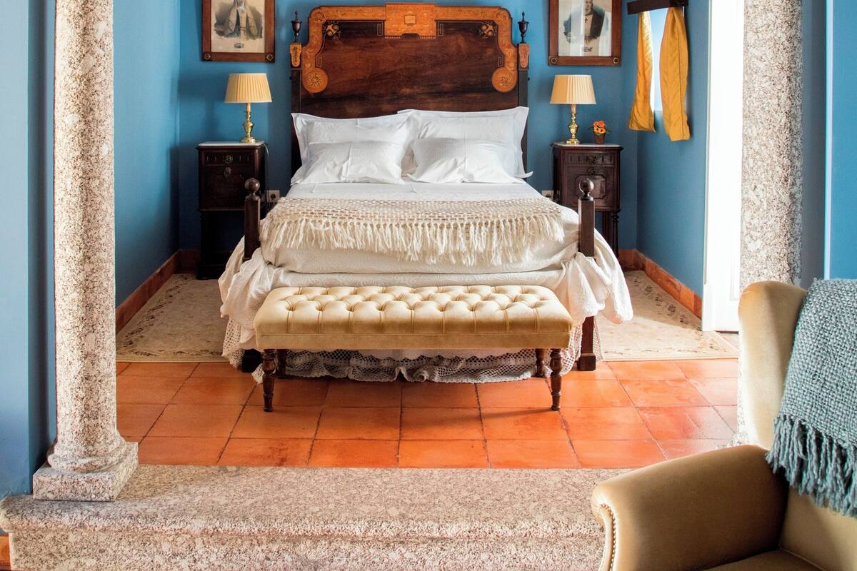 A bedroom with a large bed, two nightstands, a bench, and a chair.
