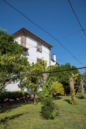 A white building with a tiled roof, surrounded by greenery and a clear blue sky.