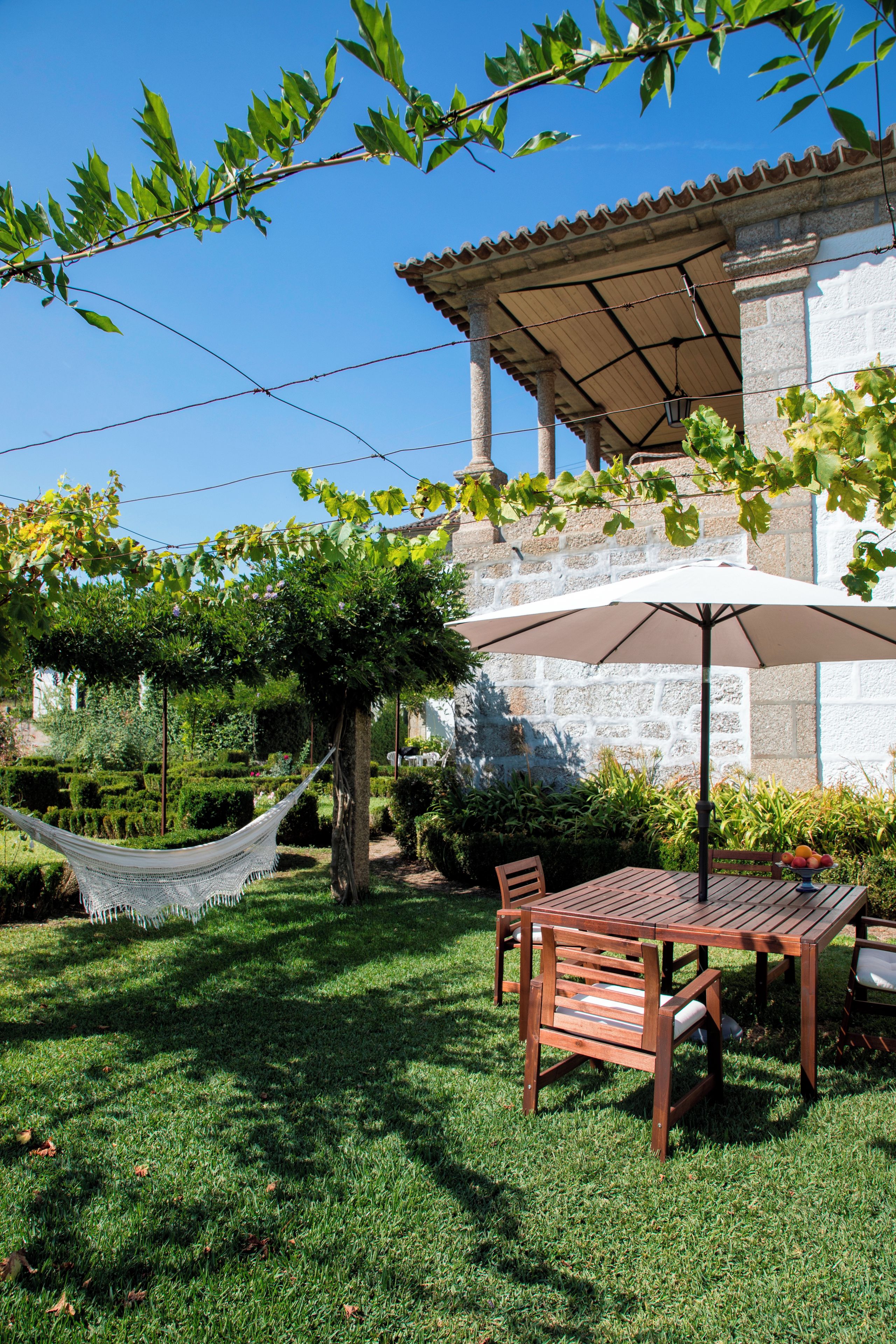 A patio with a table and chairs, a hammock, and a pergola with a white umbrella.