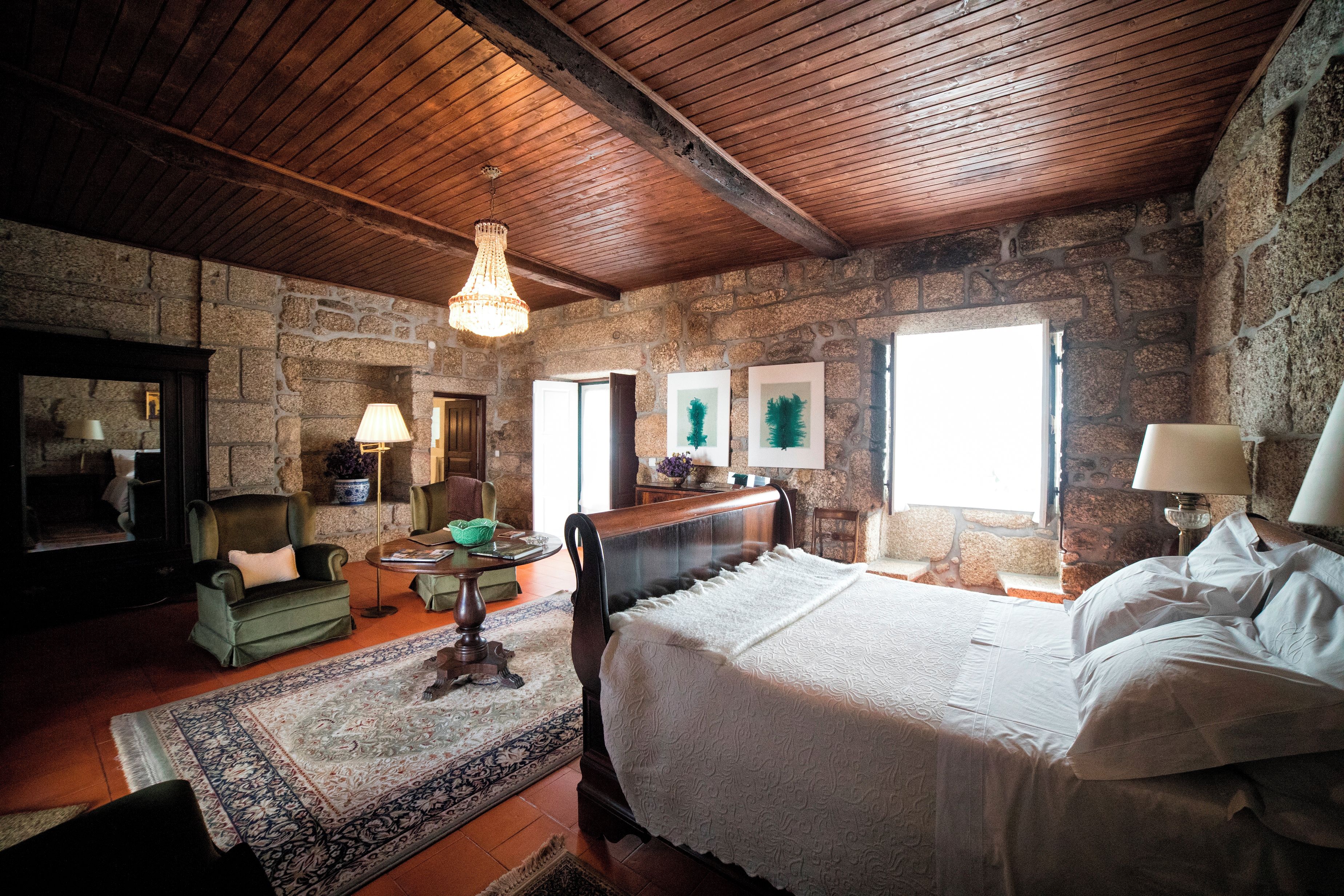 A rustic bedroom with a stone wall, wooden ceiling, and a large bed with white linens.