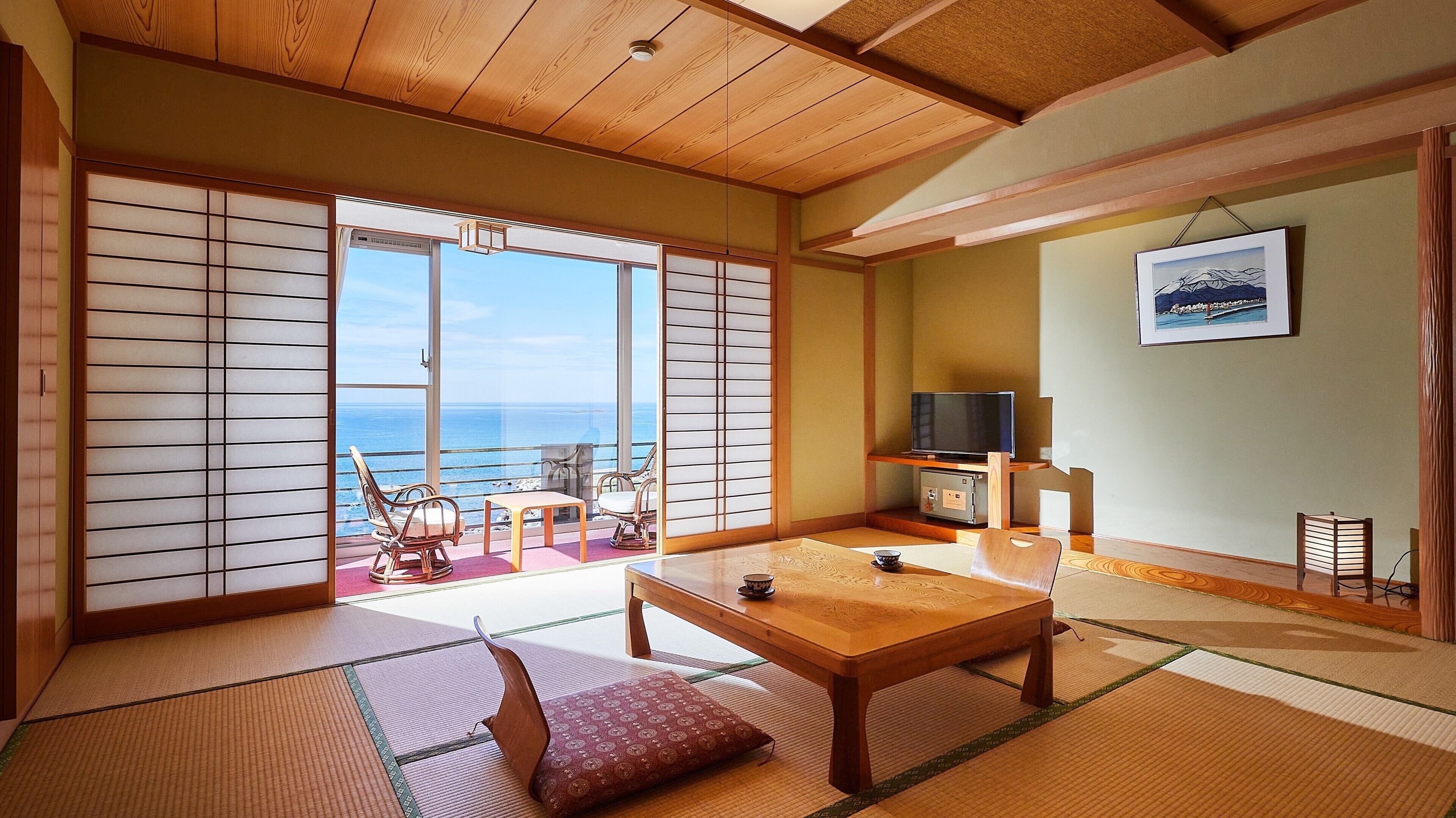 A traditional Japanese room with tatami flooring, a sliding door with a view of the sea, a television, and a framed picture on the wall.