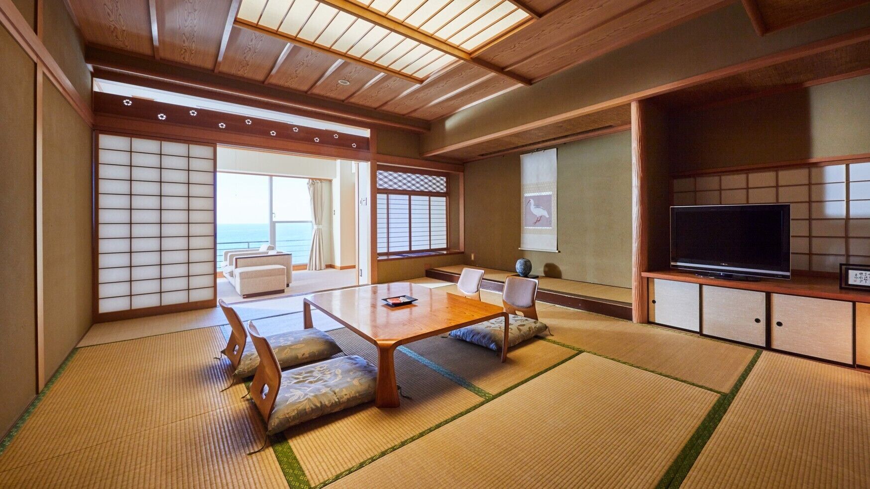A traditional Japanese room with tatami flooring, a low table, chairs, a television, and sliding doors.