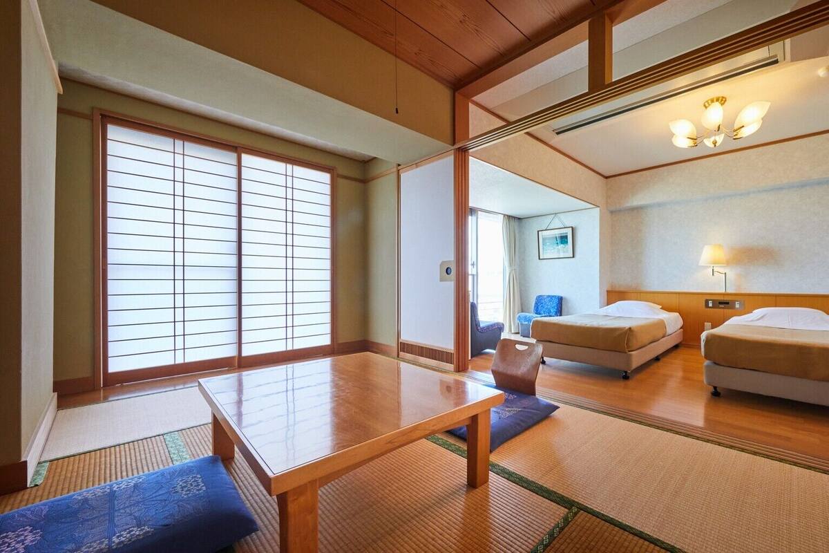 Una habitación de hotel tradicional al estilo japonés, con suelo de tatami, una mesita baja, dos camas y puertas correderas.