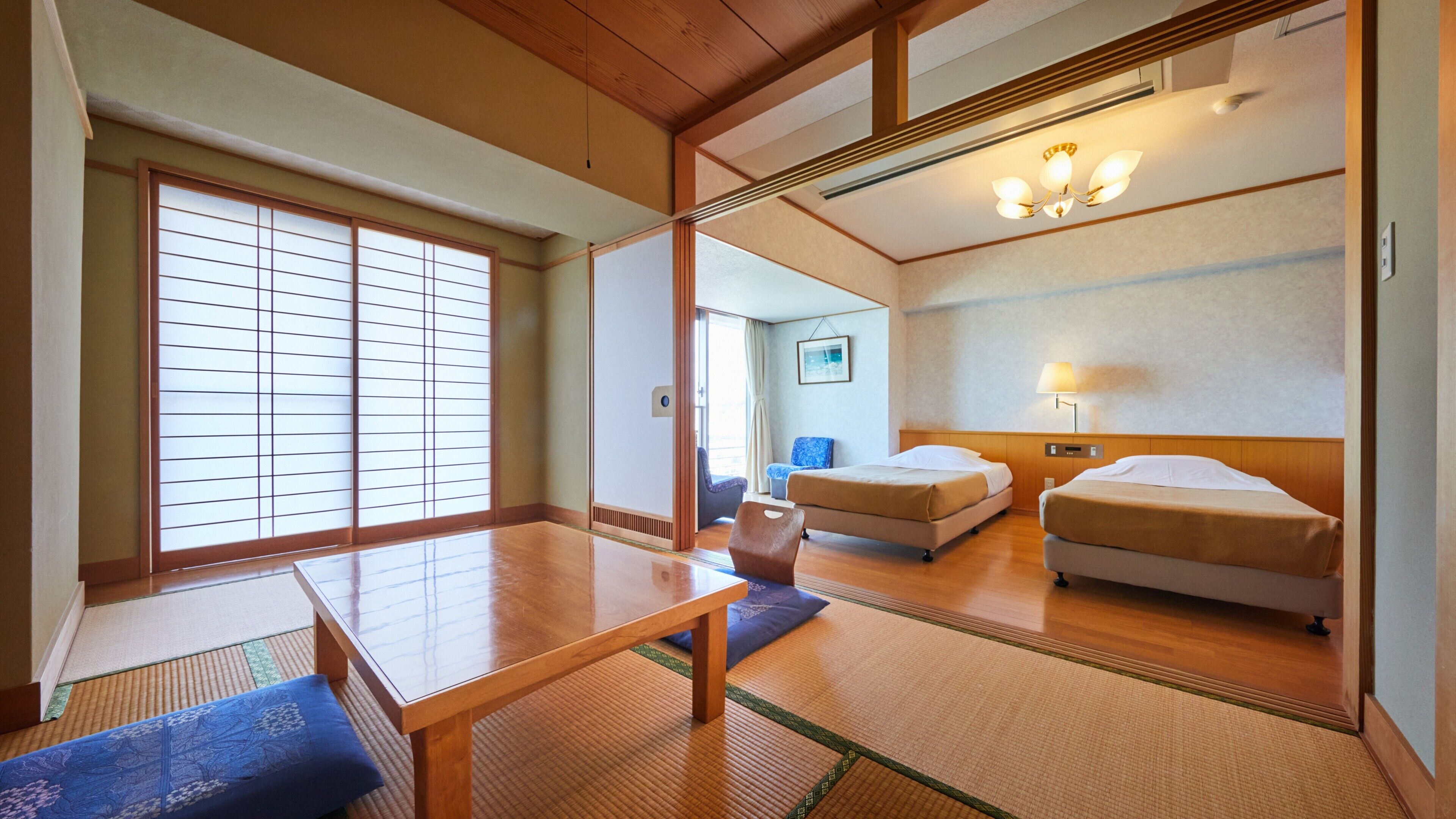 A traditional Japanese-style hotel room with tatami flooring, a wooden table, two beds, and a sliding shoji screen.