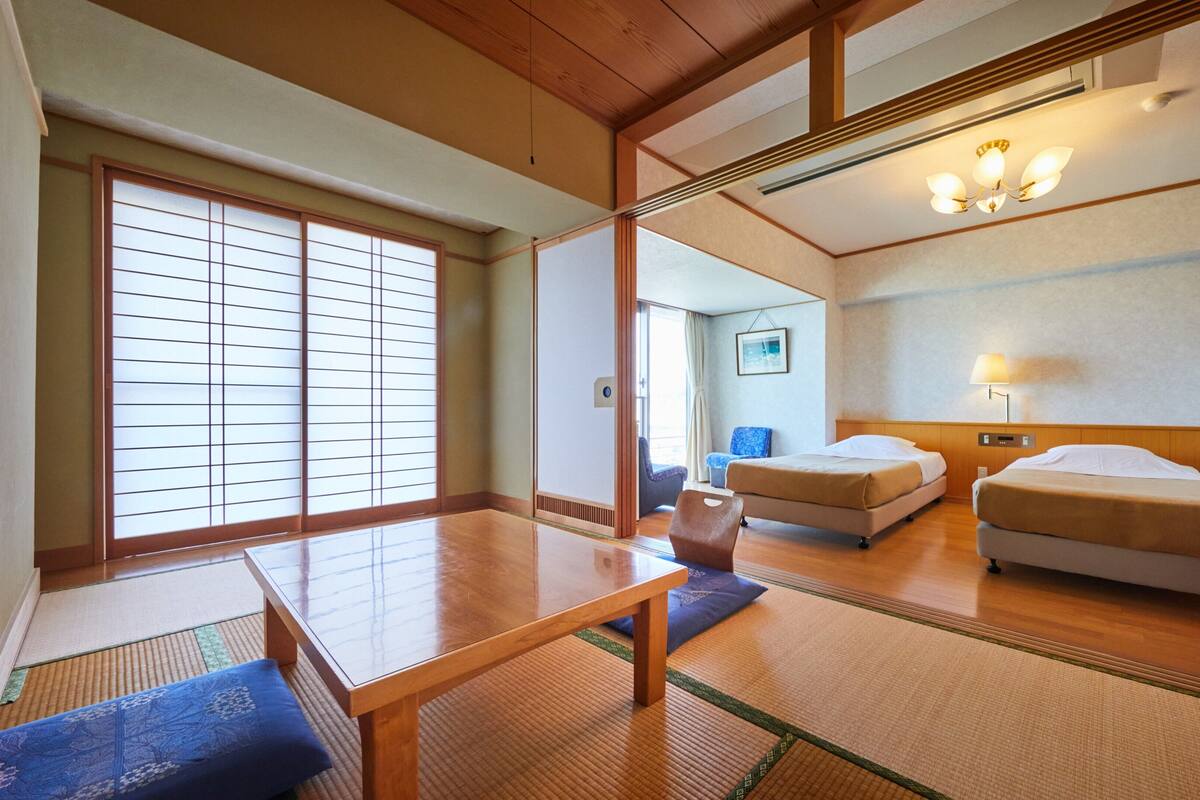 Habitación de hotel de estilo japonés tradicional, con suelo de tatami, una mesa de madera, dos camas y un panel corredizo shoji.