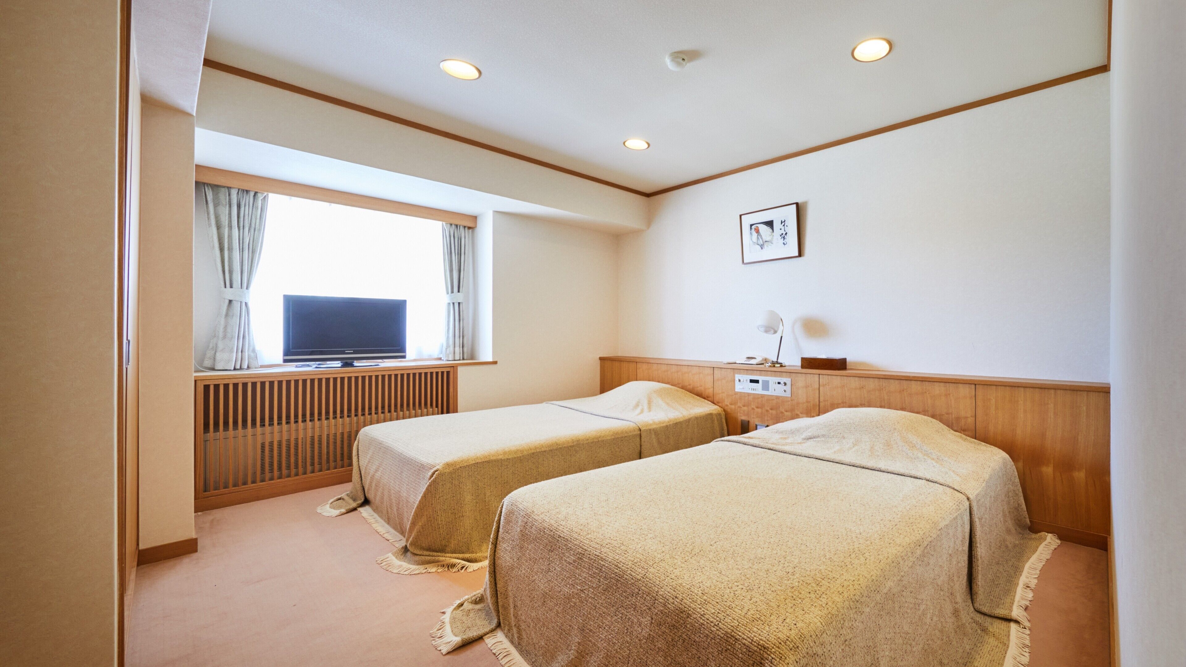 A hotel room with two beds, a TV, a desk with a lamp, and a window with curtains.